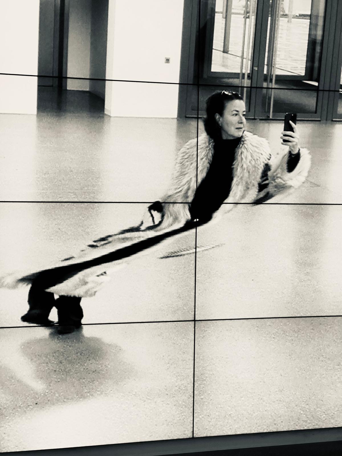 Photographer Stephanie Waldstein in a white coat, black and white self-portrait in a video wall